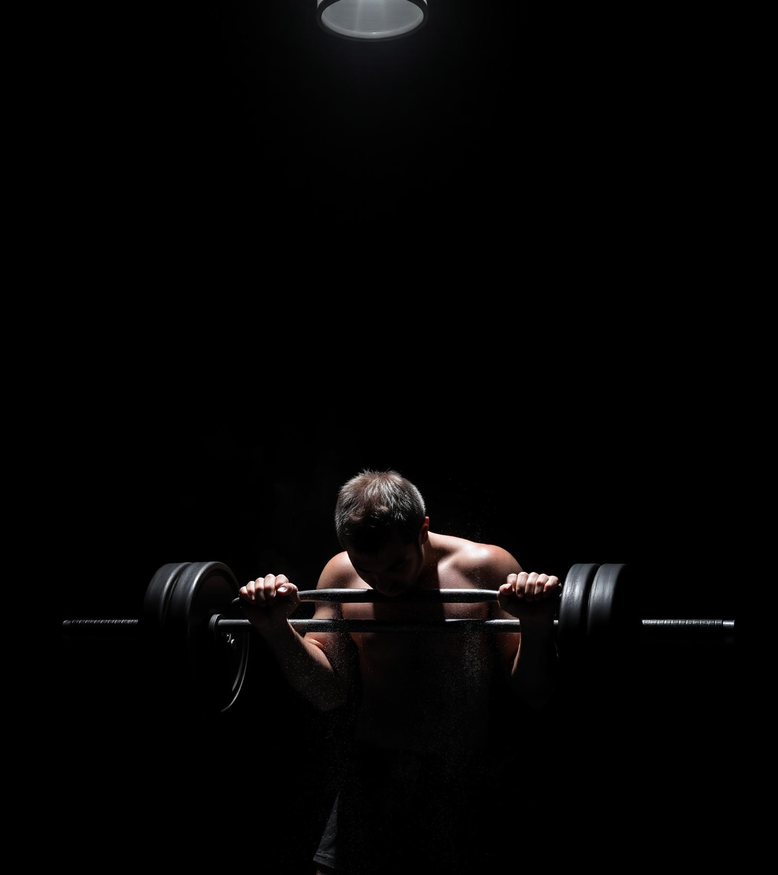 Athlete lifting heavy barbell under a single spotlight